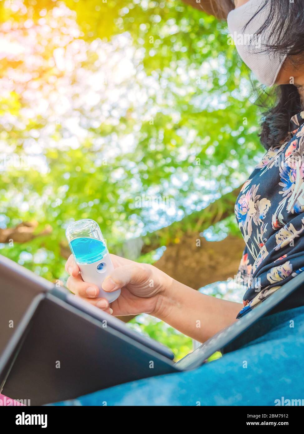Frau trägt Schutzmaske mit Alkohol Nano Sprüher Reinigung eines Laptops