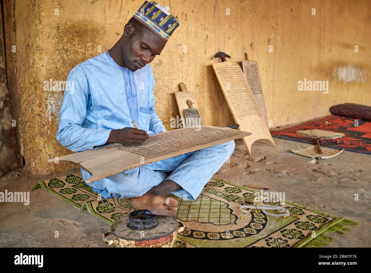 Muslimischer Mann, der korankalligraphie auf einer Holztafel praktiziert. Stockfoto