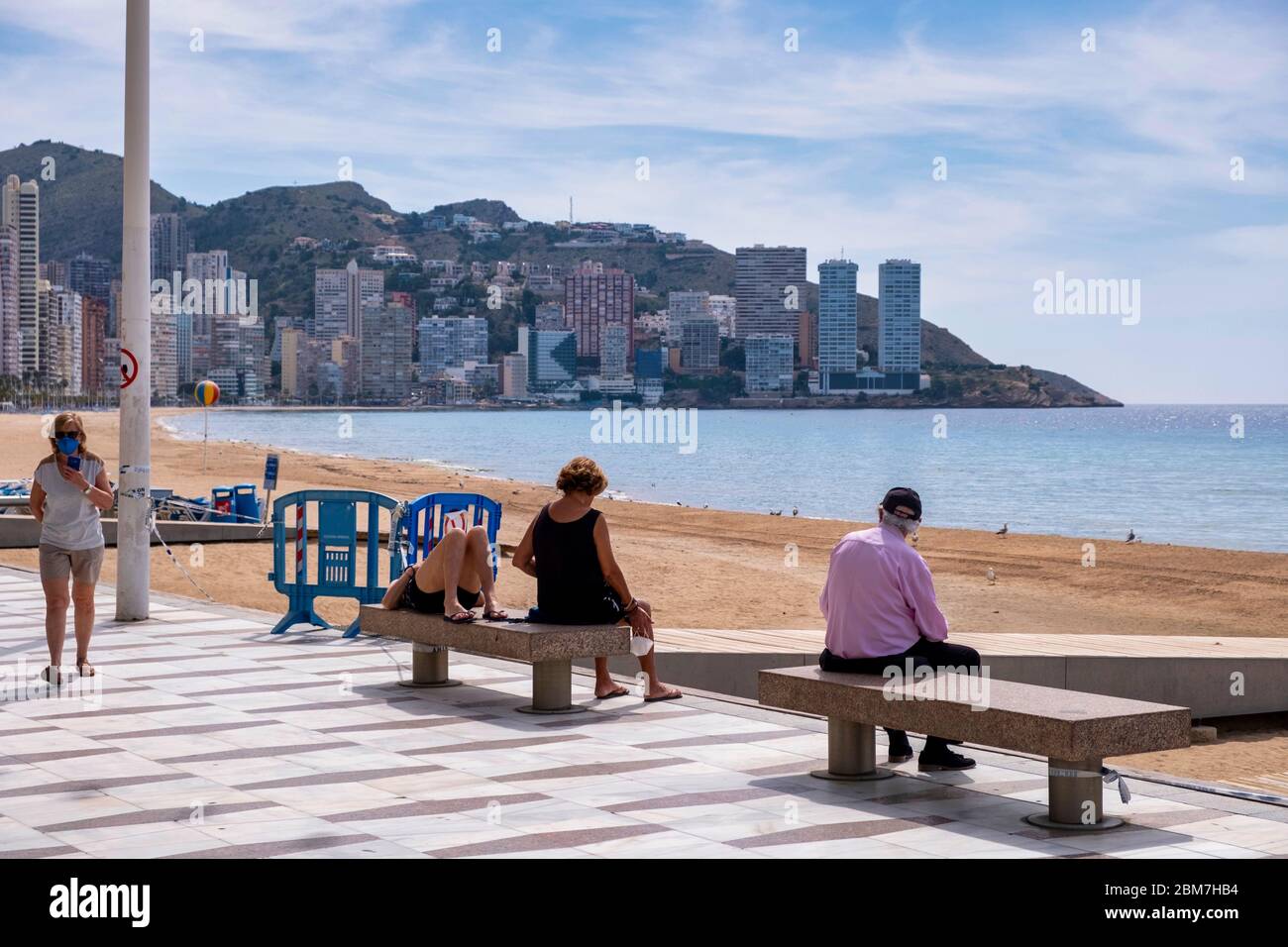 Benidorm, Alicante Spanien, 4.5.2020, Corona-Krise: Drei Leute sitzen und liegen auf Steinbänken an der Promenade am menschenleeren Strand Playa Levante Stockfoto