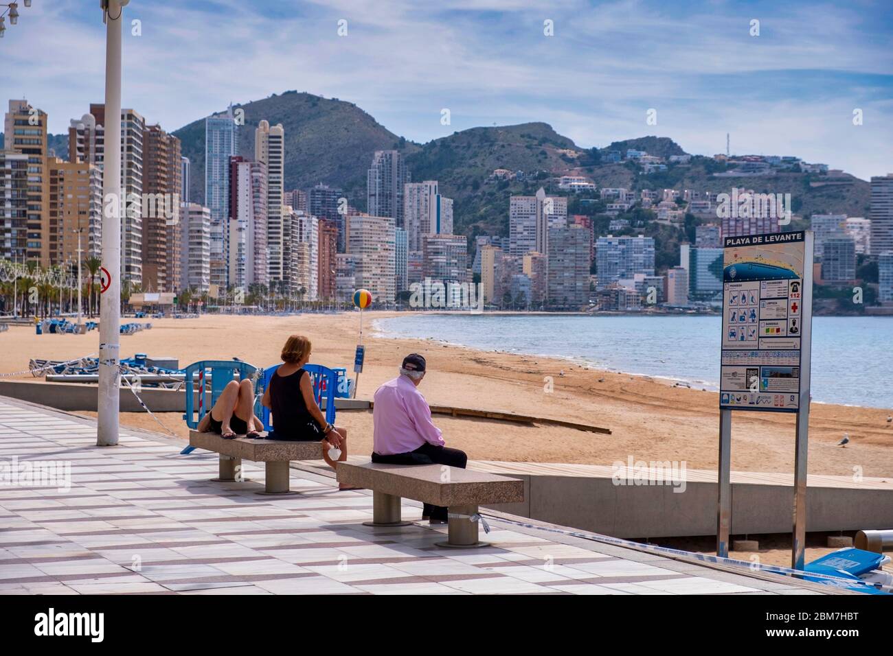 Benidorm, Alicante Spanien, 4.5.2020, Corona-Krise: Drei Leute sitzen und liegen auf Steinbänken an der Promenade am menschenleeren Strand Playa Levante Stockfoto