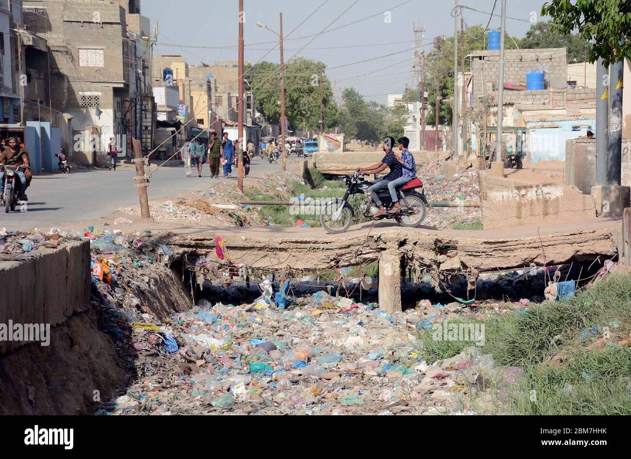 Pendler überqueren offene Abfluss durch die Verwendung einer beschädigten Brücke kann Lebensgefahr für sie, dass füllt sich mit Müll, die die Nachlässigkeit der betroffenen Behörden, auf Korangi Gebiet von Karachi am Donnerstag, 7. Mai 2020. Stockfoto