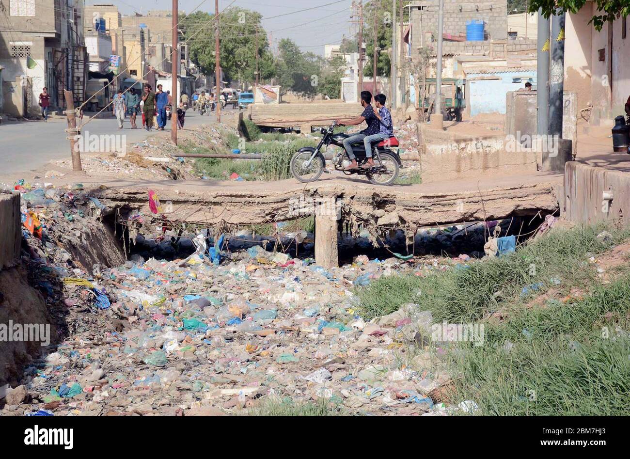 Pendler überqueren offene Abfluss durch die Verwendung einer beschädigten Brücke kann Lebensgefahr für sie, dass füllt sich mit Müll, die die Nachlässigkeit der betroffenen Behörden, auf Korangi Gebiet von Karachi am Donnerstag, 7. Mai 2020. Stockfoto