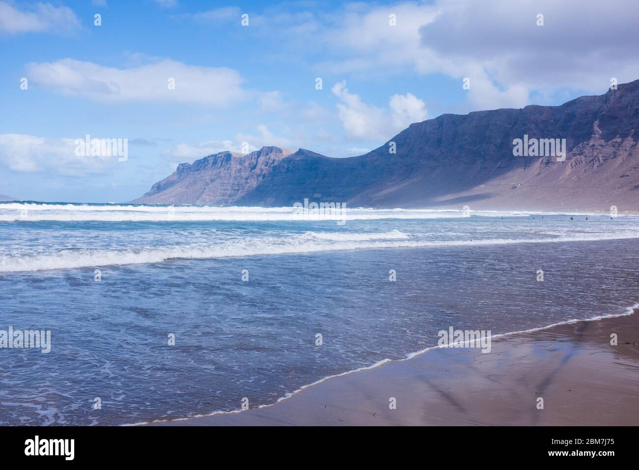 Wellen umrunden den Strand mit einer spektakulären Klippenkulisse in der beliebten Wassersportstation Caleta de Famara auf Lanzarote, Kanarische Inseln Stockfoto