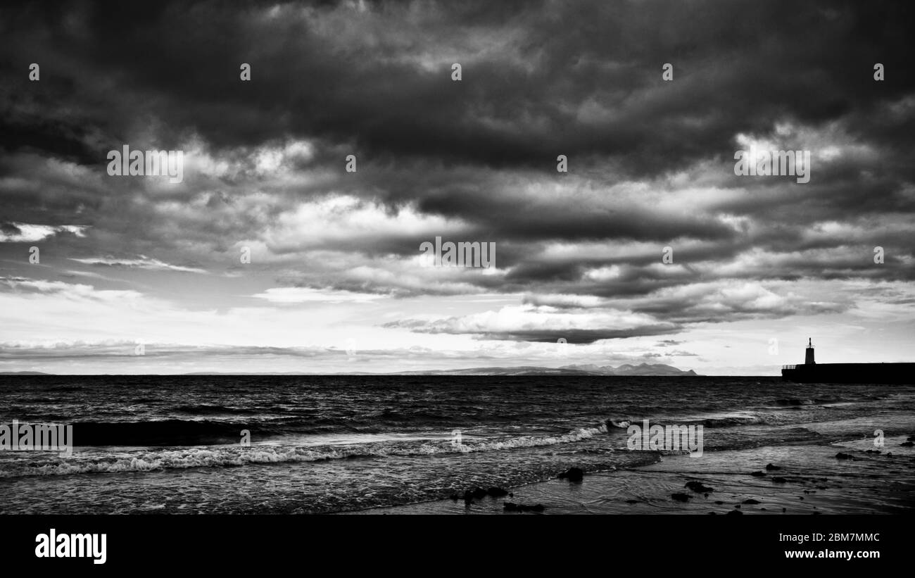 Schwarz-Weiß-Bild, wie die Flut dreht Wellen sanft brechen. Der Horizont gefüllt mit dramatischen dunklen Wolken, schottische Küste, Schottland Stockfoto