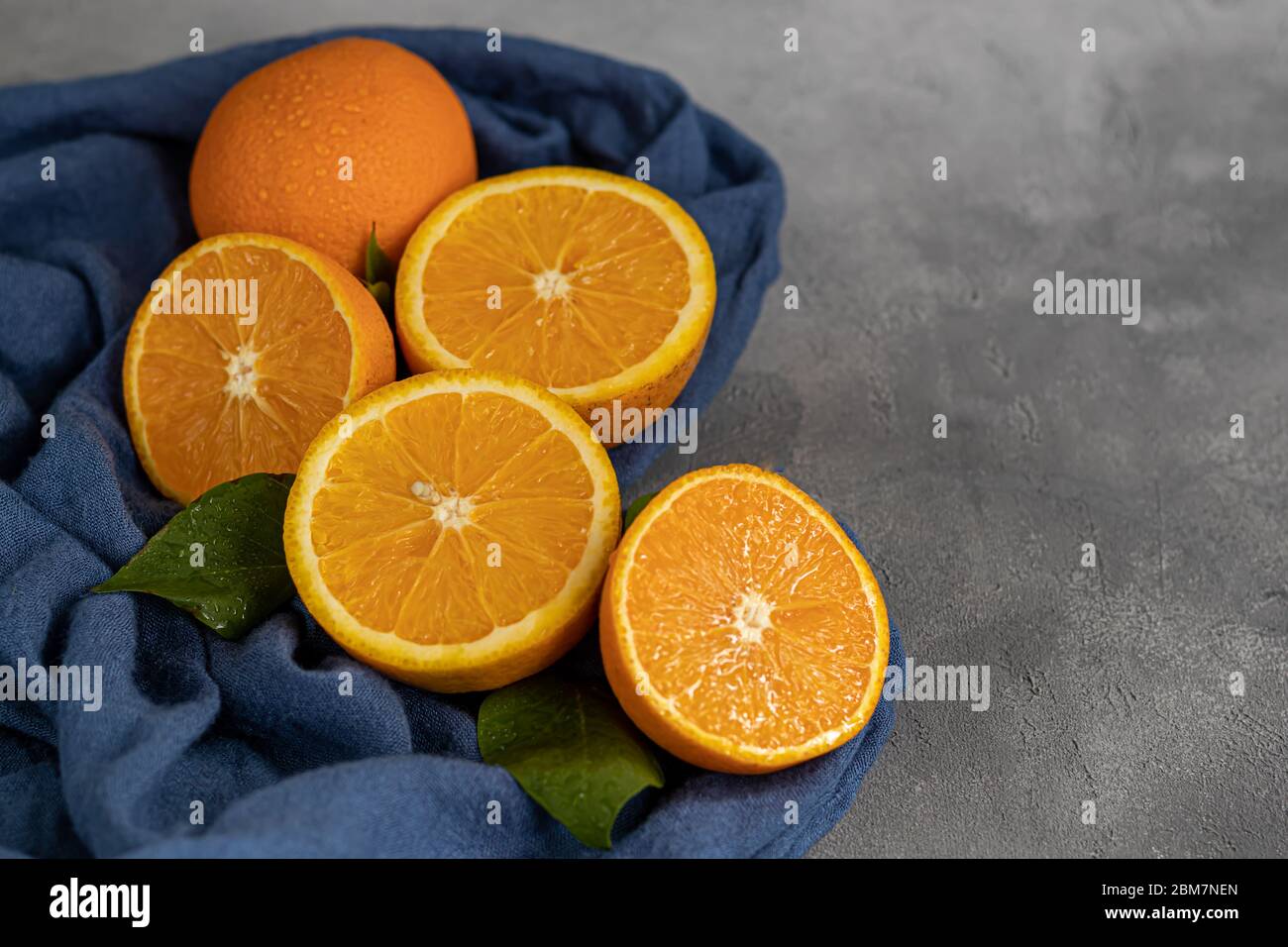 Reife frische Orangen in zwei Hälften geschnitten auf einem blauen Tuch. Garniert mit Zimtstangen, Nelkensamen und grünen Blättern. Das Konzept der Vitamine für Viren. Stockfoto