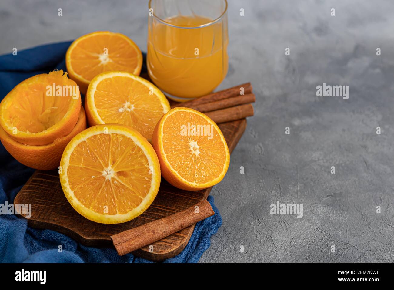 Reife frische Orangen in zwei Hälften geschnitten auf einem blauen Tuch. Garniert mit Zimtstangen, Nelkensamen und grünen Blättern. Das Konzept der Vitamine für Viren. Stockfoto