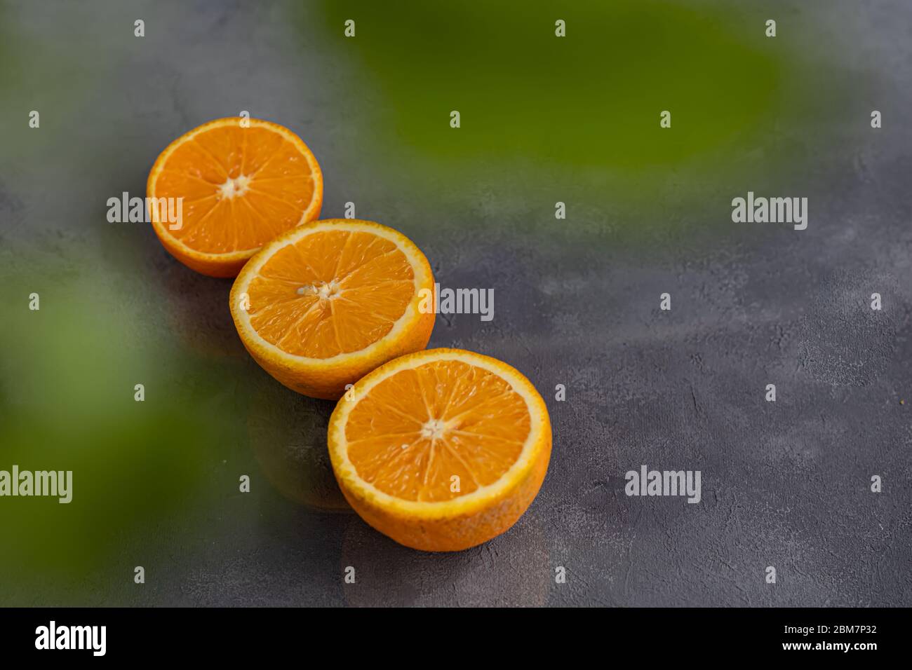 Reife frische Orangen in zwei Hälften geschnitten auf einem blauen Tuch. Garniert mit Zimtstangen, Nelkensamen und grünen Blättern. Das Konzept der Vitamine für Viren. Stockfoto