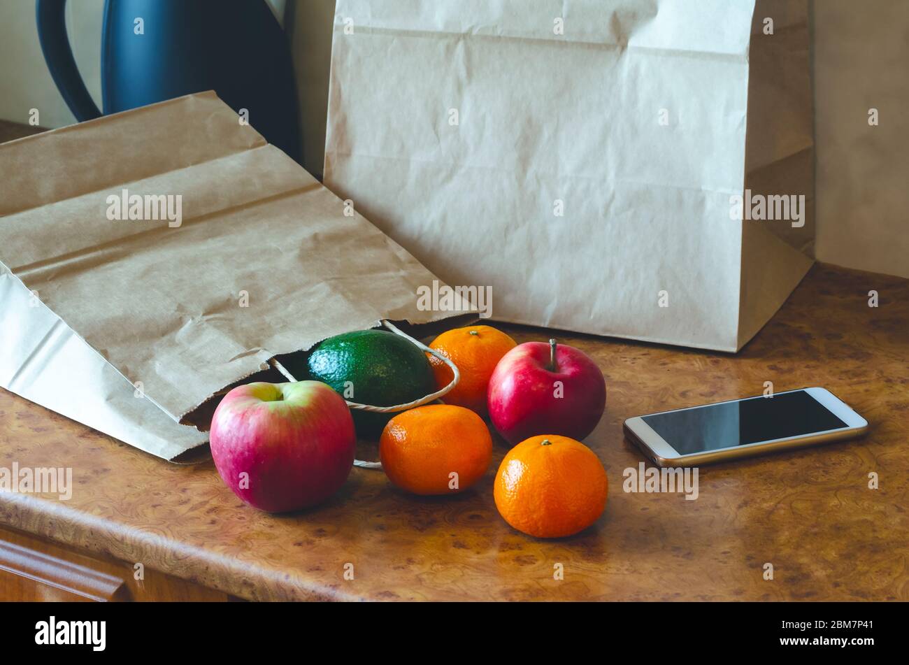 Papiertüten, frisches Gemüse und Obst neben einem Mobiltelefon auf dem Tisch mit Küchenutensilien. Online-Shopping und kontaktloses Lieferkonzept. Stockfoto