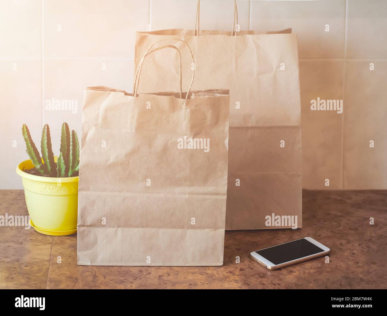 Papiertüten, Handy und eine Zimmerpflanze in einem gelben Topf auf einem Küchentisch. Online-Shopping und kontaktloses Lieferkonzept. Stockfoto