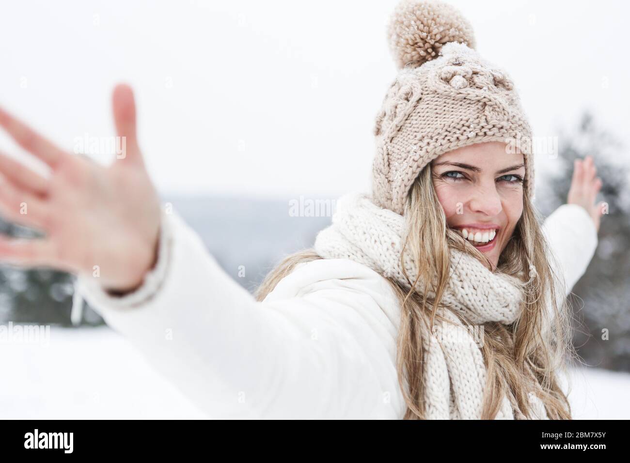 Lachende Frau steht im Winter mit ausgestreckten Armen im Schnee Stockfoto