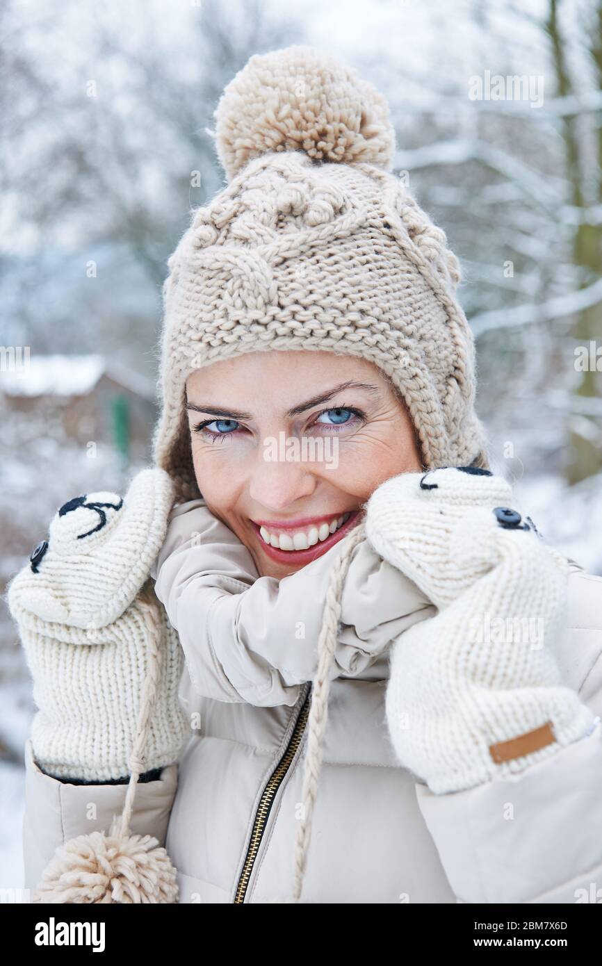 Lachende Frau steht mit Bommel Hut im Schnee im Winter Stockfoto