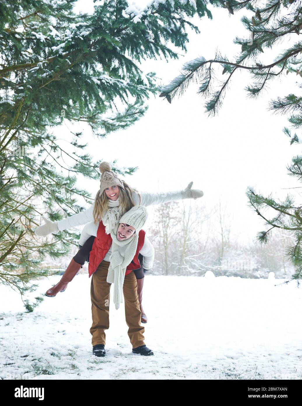 Lachender Mann Huckepack glückliche Frau im Winter durch Schnee Stockfoto