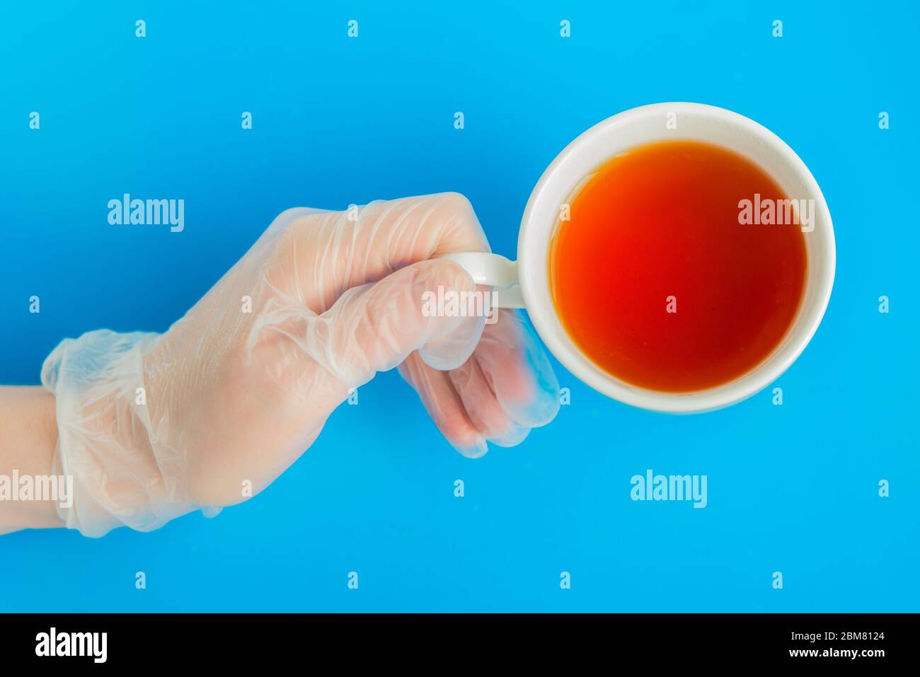 Doctor Hand in medizinischen Handschuh hält weißen Tee Tasse auf dem blauen Hintergrund Flatlay Stockfoto