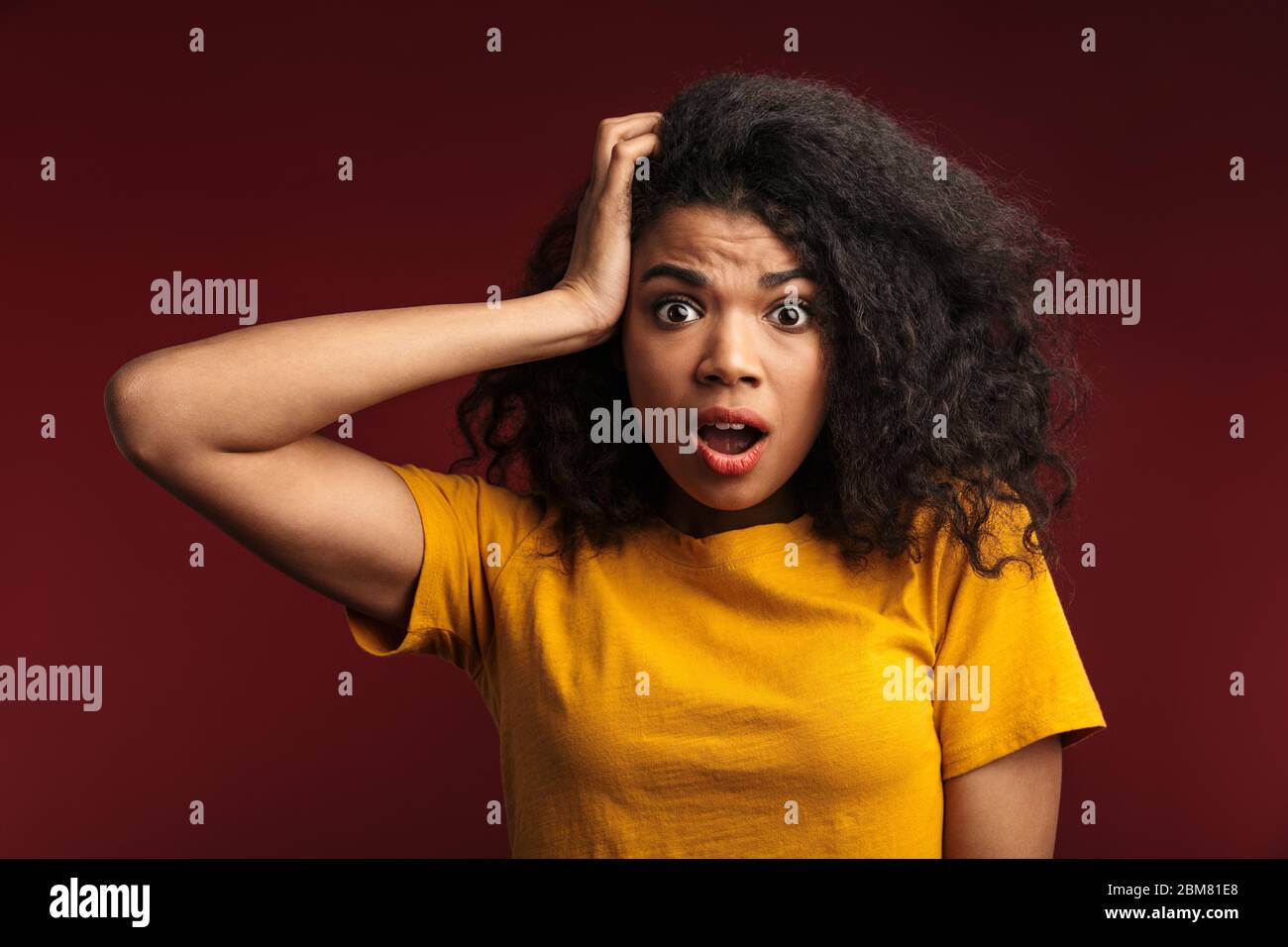 Bild von schockiert emotional verwirrt junge afrikanerin posiert isoliert über dunkelroten Wand Hintergrund. Stockfoto