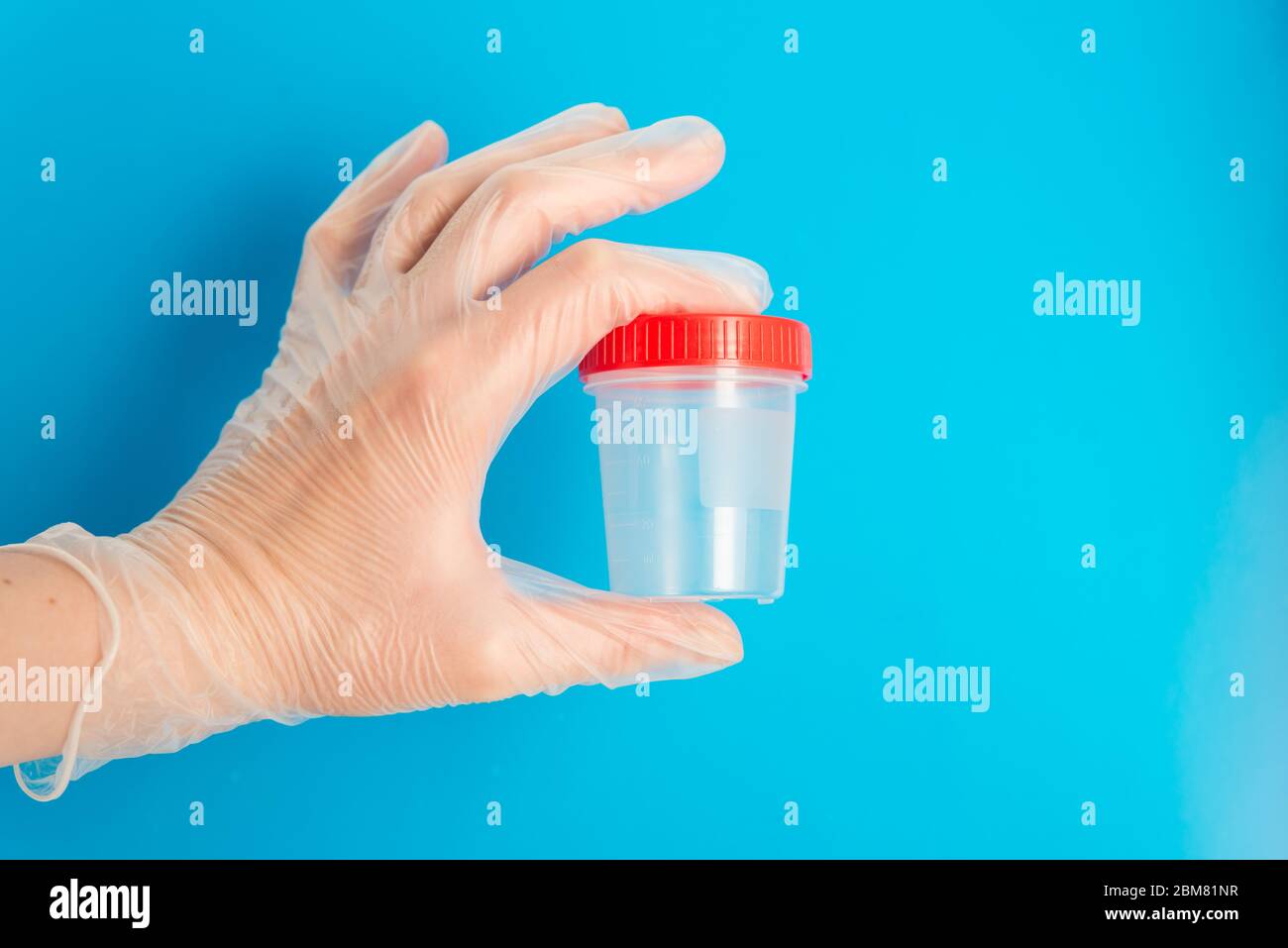 Doctor Hand in medizinischen Handschuh hält einen leeren Plastikbehälter für Tests auf einem blauen Hintergrund mit Kopierraum Stockfoto
