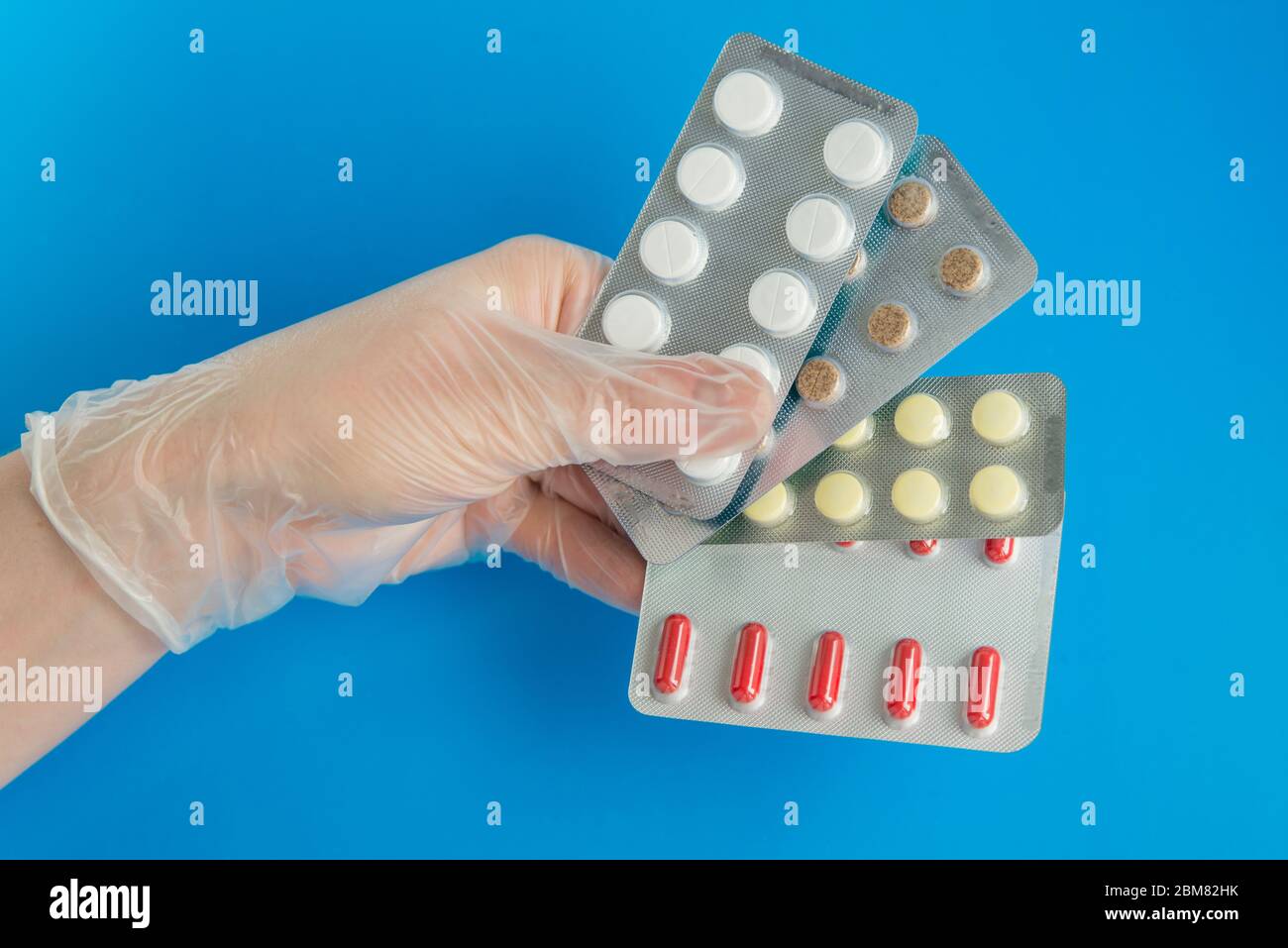 Hand in einen Schutzhandschuh mit ein paar Tabletten Packs auf dem blauen Hintergrund Stockfoto