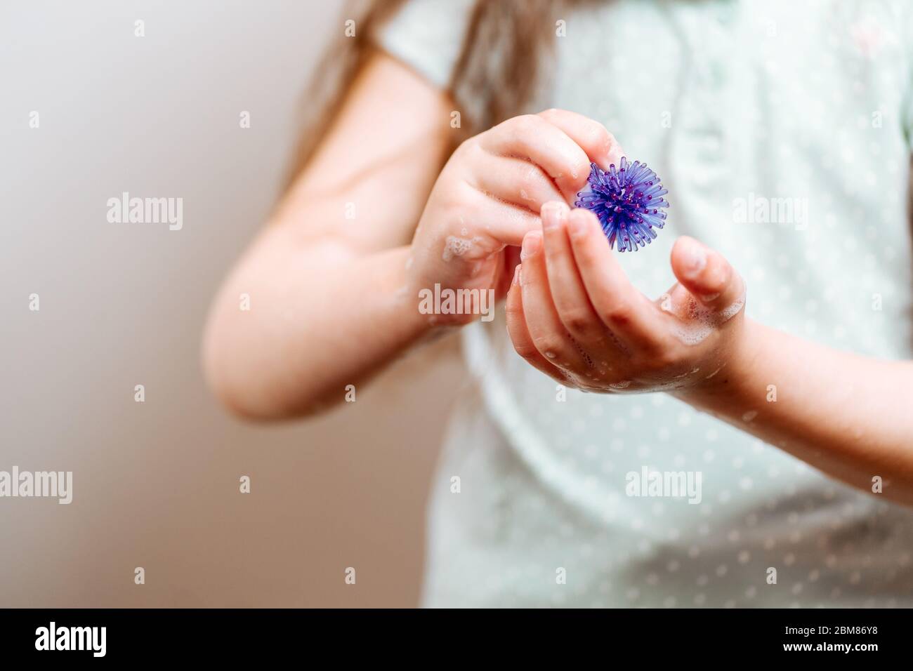 Mädchen mit Händen in Seife hält ein abstraktes Modell des Coronavirus. Schützen Sie sich waschen Sie Ihre Hände häufiger. Stockfoto