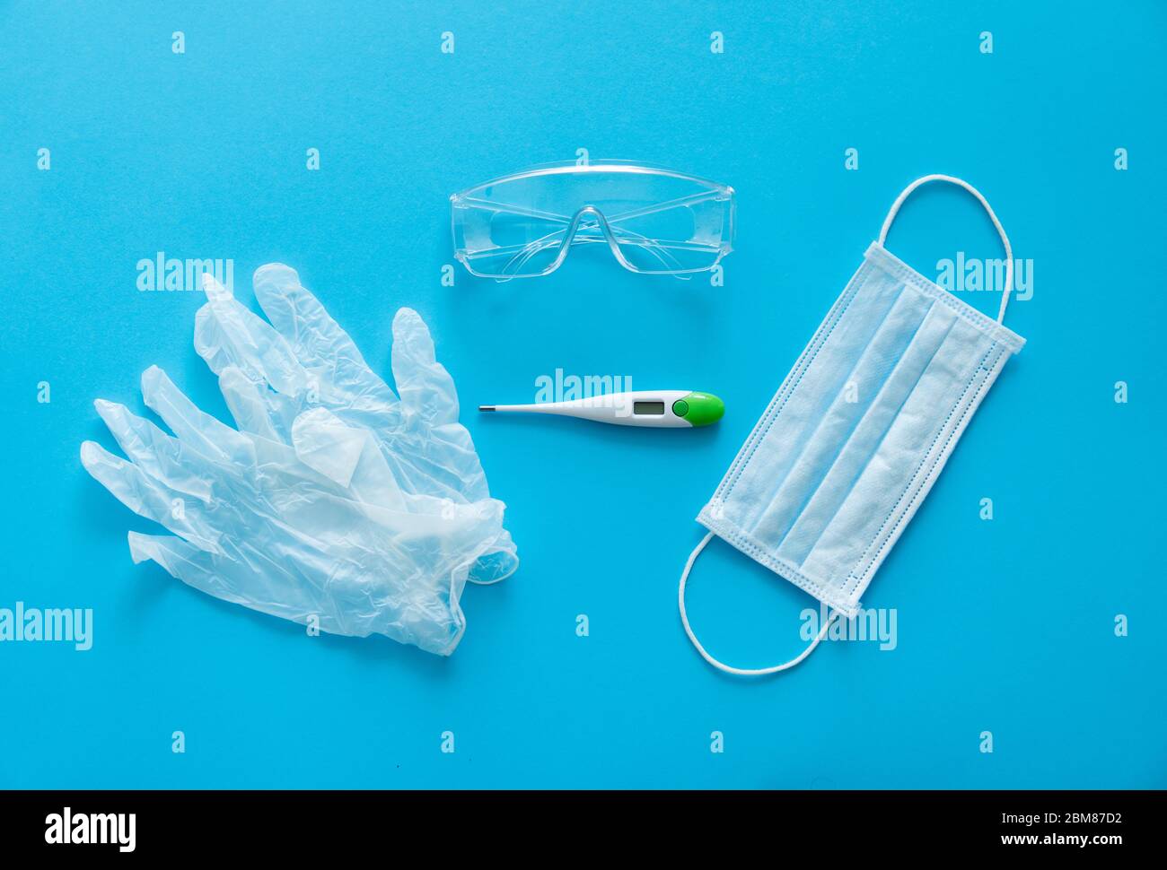 Medizinische Schutzmaske, Gummihandschuhe, Thermometer und Schutzbrille liegen auf blauem Hintergrund. Anti-Virus-Schutz-Kit gegen covid-19. Coron Stockfoto