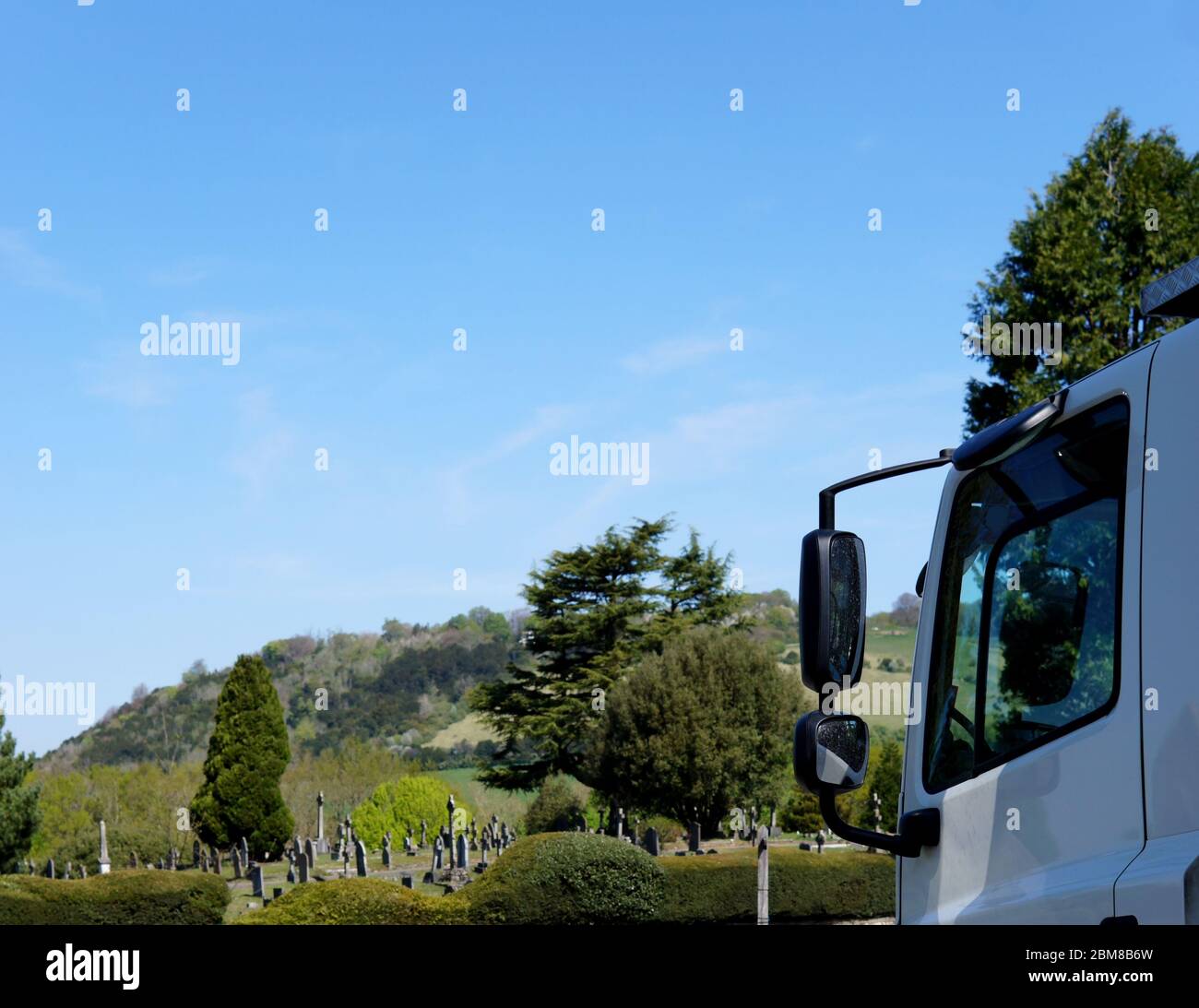 Die Vorderseite eines Lastwagens, zeigt die Fahrzeuge in der Nähe schmutzige Tür und Flügel Spiegel mit einem Transport Sicherheit Botschaft eines verschwommenen Friedhof und Ökologie Stockfoto