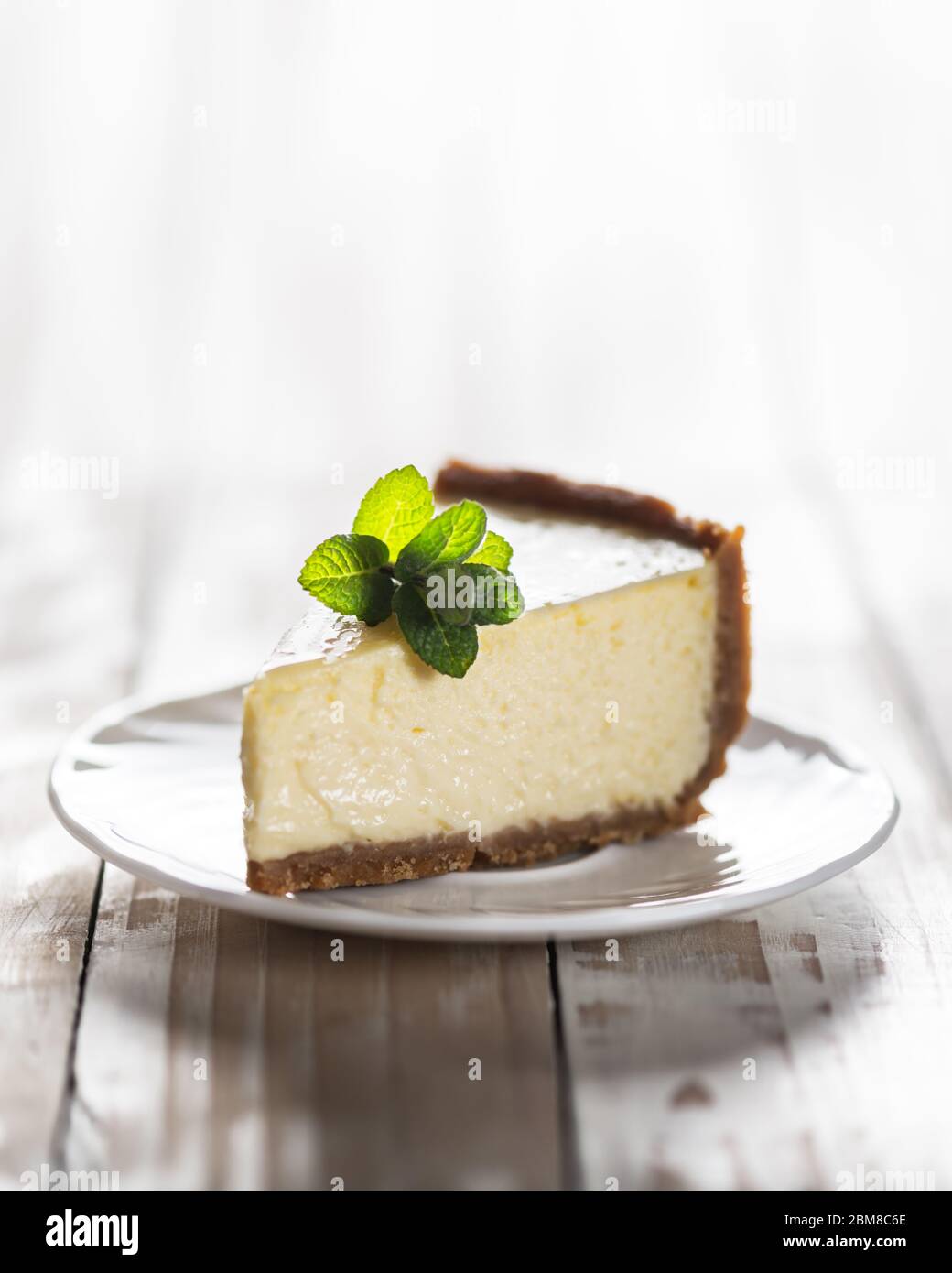 Ein Stück klassischer New Yorker Käsekuchen mit einem Zweig Minze auf einem Teller auf einem Holztisch. Das Konzept der Bäckerei und Süßspeisen Desserts Stockfoto