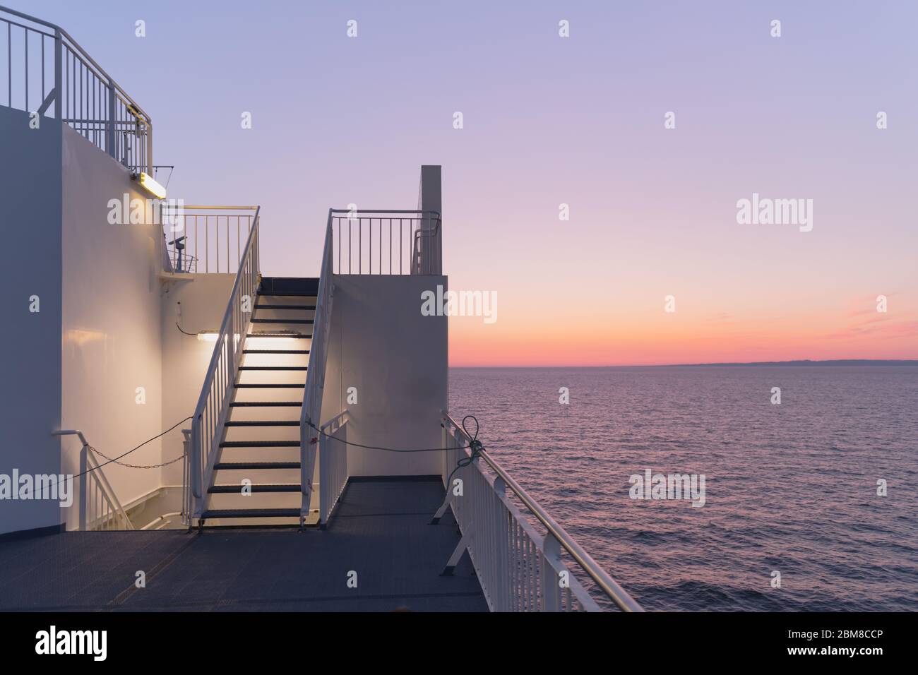 Deck eines Kreuzfahrtschiffes bei Sonnenuntergang. Ruhiges Meer und klarer rosa Himmel am Abend. Kreuzfahrt Urlaub Hintergrund. Minimalismus in der Fotografie Stockfoto