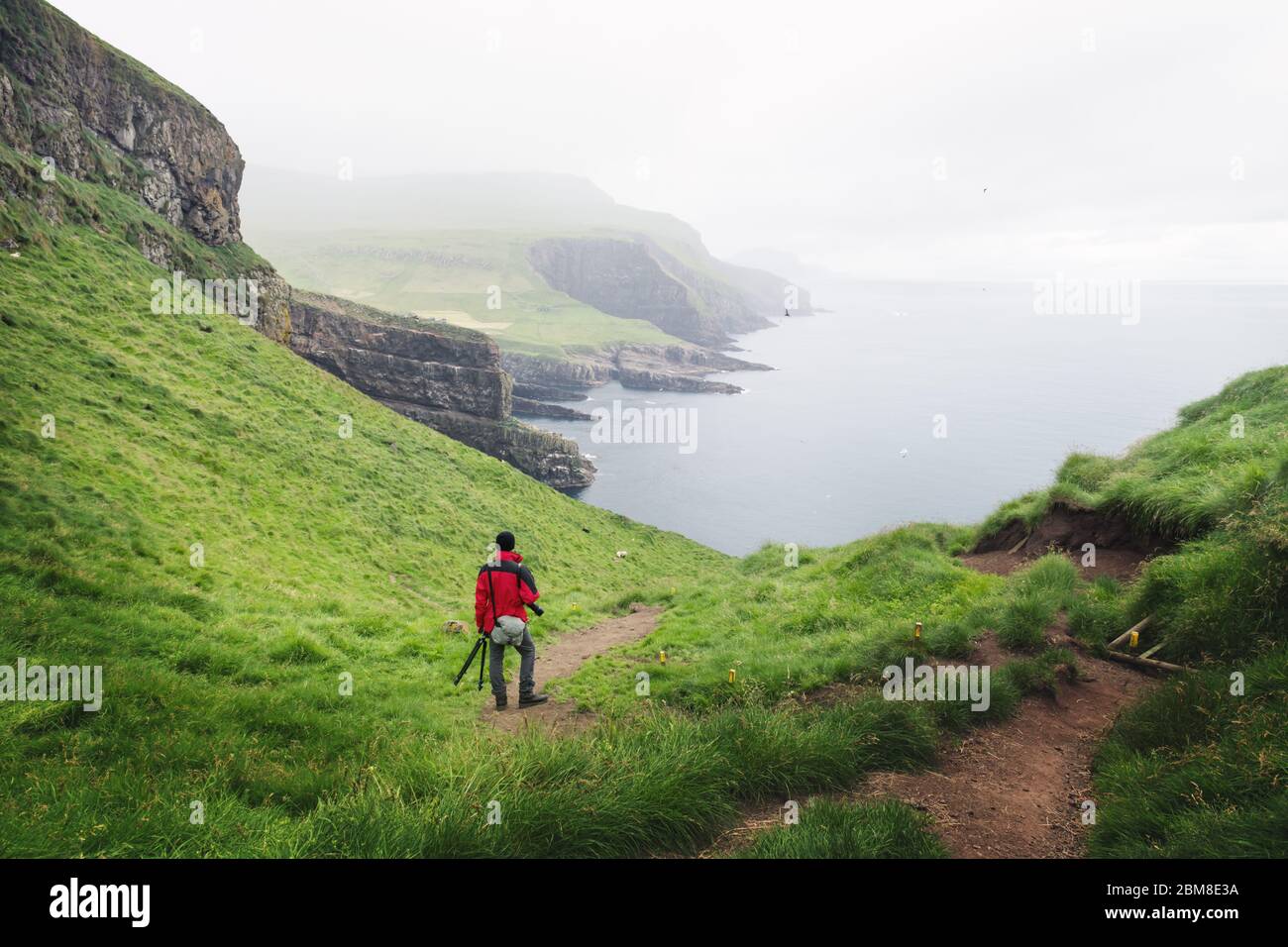 Neblige Ansicht der Insel Mykines mit Touristen in roter Jacke auf den Färöer Inseln, Dänemark. Landschaftsfotografie Stockfoto