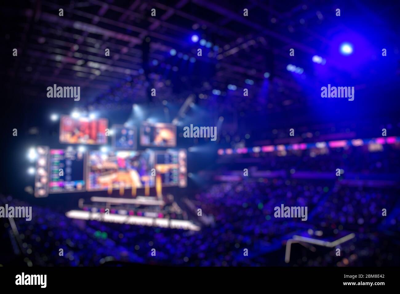 Verschwommener Hintergrund eines eSports-Events - große beleuchtete Hauptbühne eines Computerspielturniers, das sich auf einem großen Stadion befindet. Tribune sind voll Stockfoto