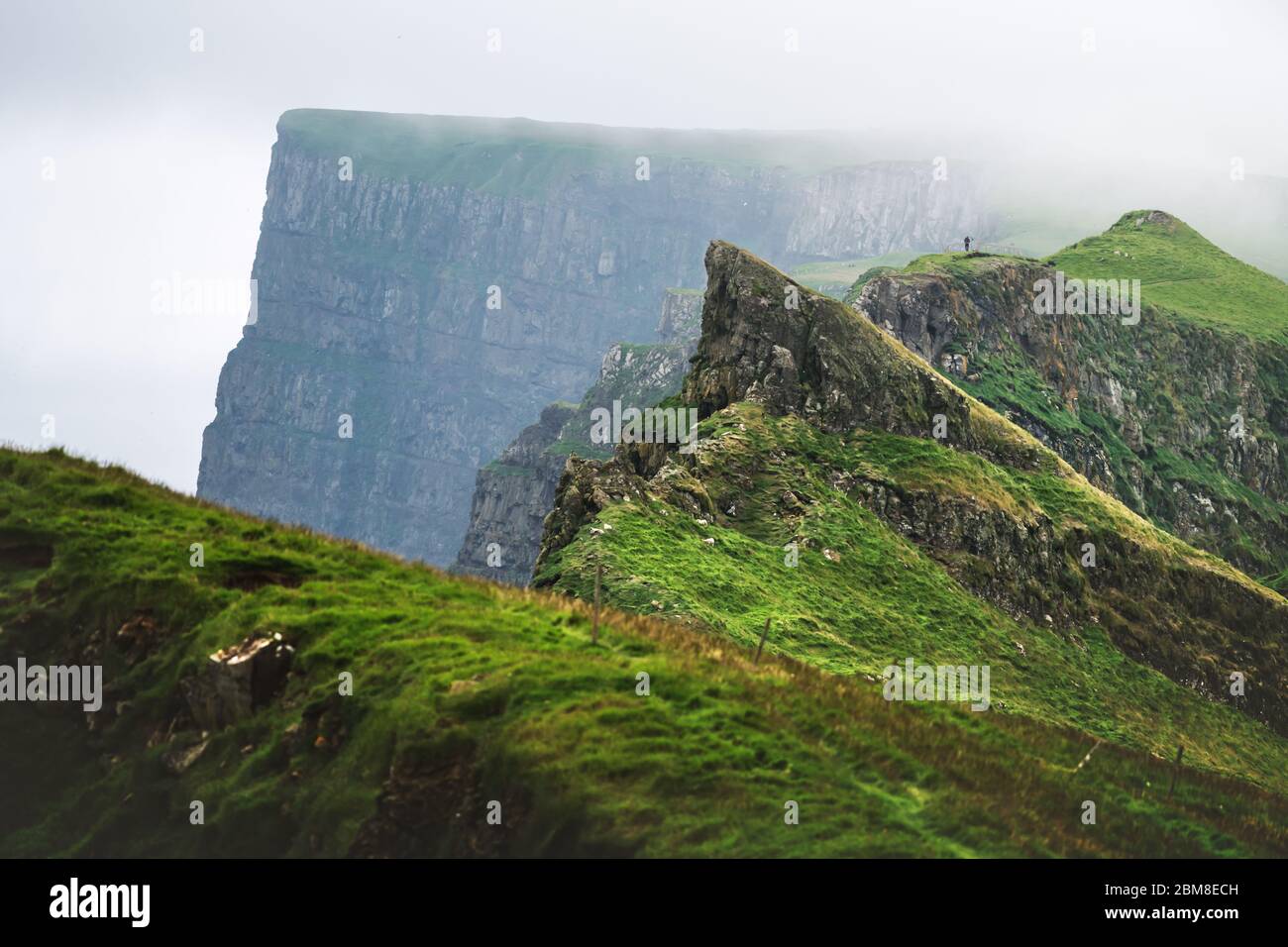 Neblige Aussicht auf die wunderschönen Berge der Insel Mykines mit Touristen auf hohem Aussichtspunkt. Färöer Inseln, Dänemark. Landschaftsfotografie Stockfoto