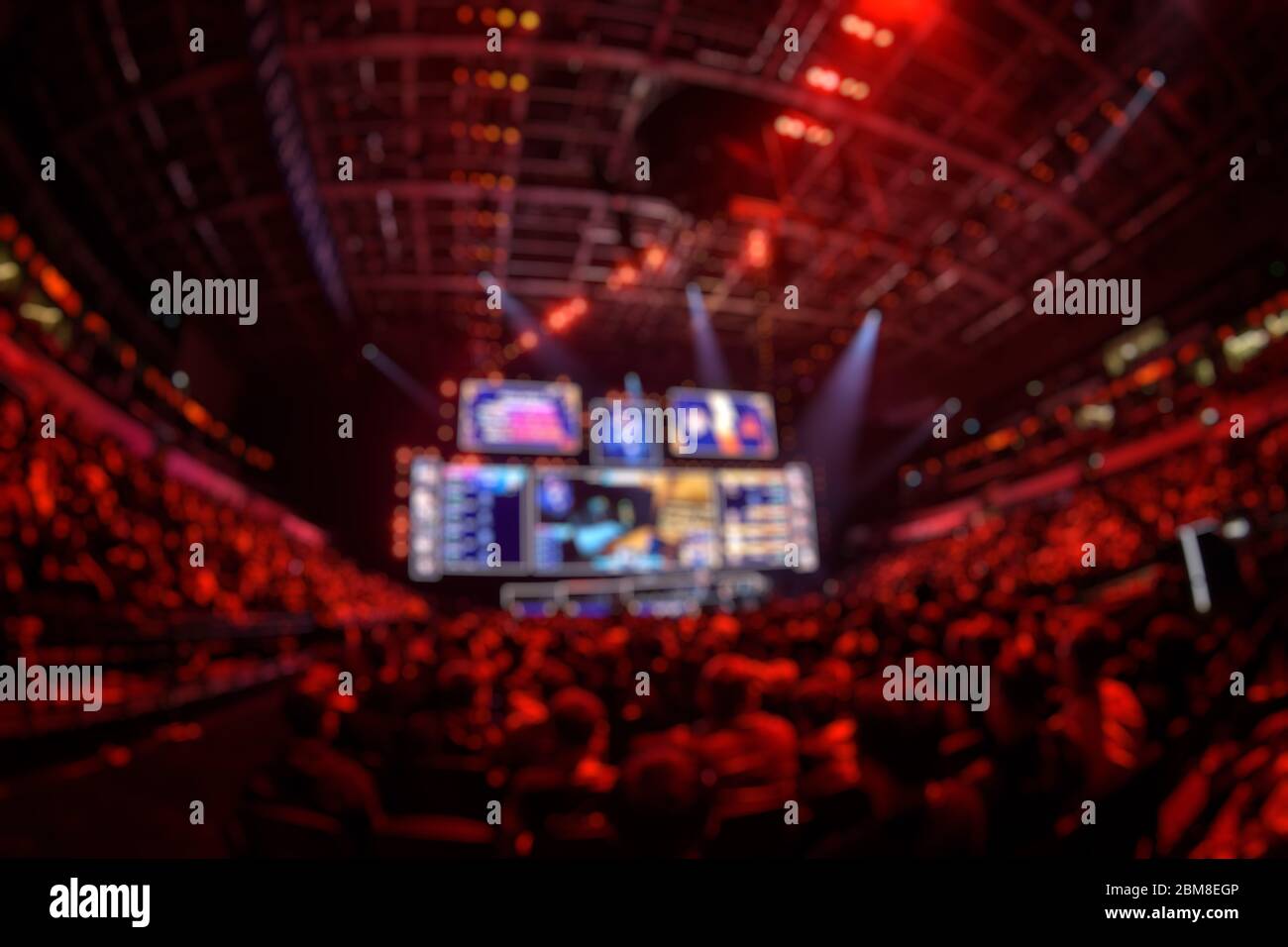 Verschwommener Hintergrund eines eSports-Events - große beleuchtete Hauptbühne eines Computerspielturniers, das sich auf einem großen Stadion befindet. Tribune sind voll Stockfoto
