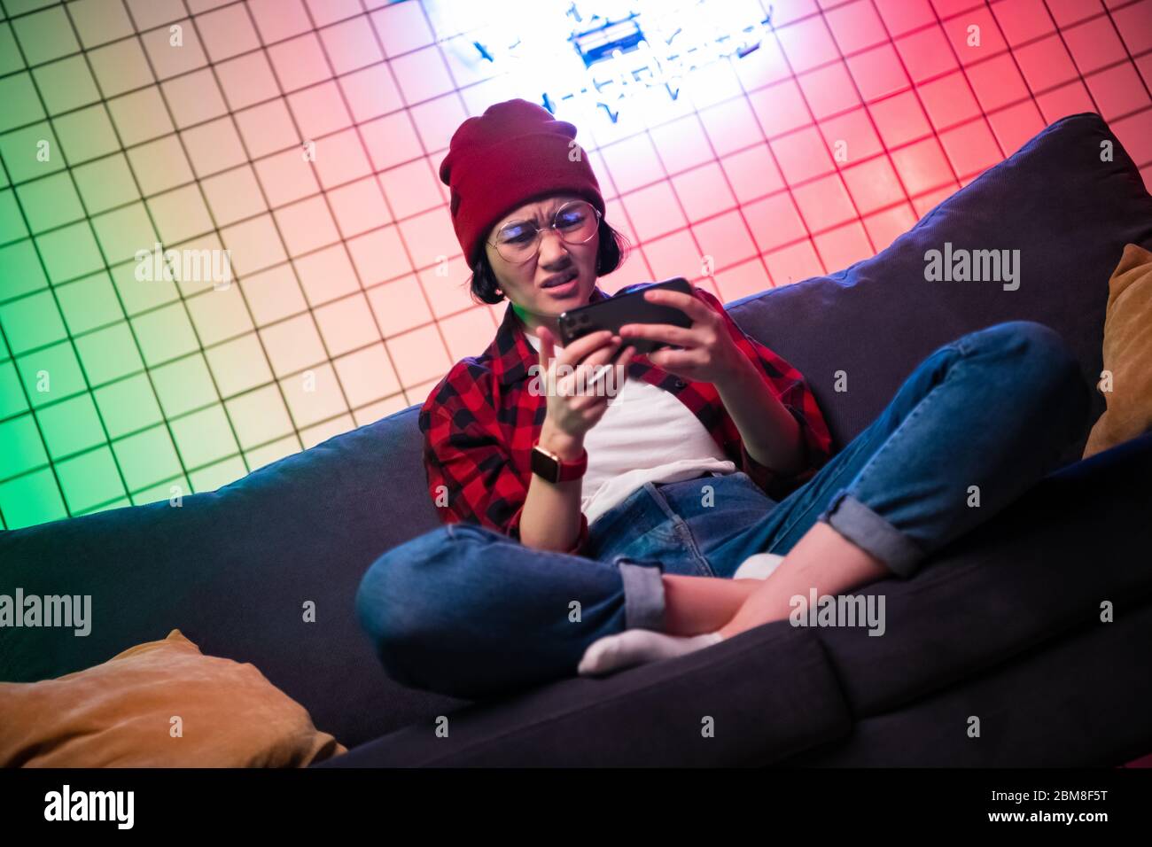 Teenager-Mädchen aufregend, das Smartphone in einem Raum spielt, der mit Neonfarbe zu Hause beleuchtet ist. Stockfoto