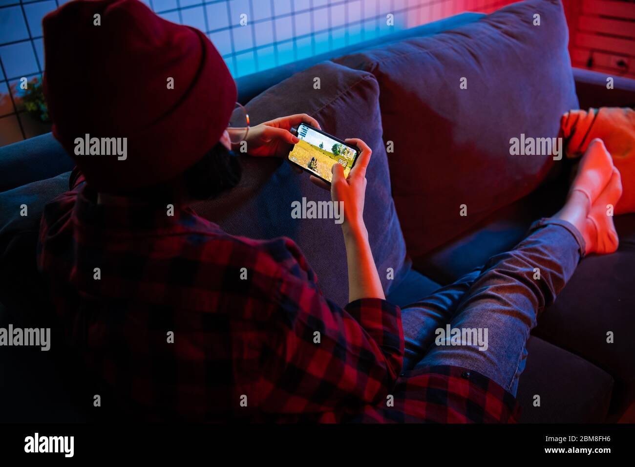 MOSKAU, RUSSLAND - 6. Dezember 2019: Seitenansicht eines Teenagers, der in der Nacht zu Hause auf einem Smartphone auf einem Sofa liegt und PUBG Online-Spiel spielt Stockfoto