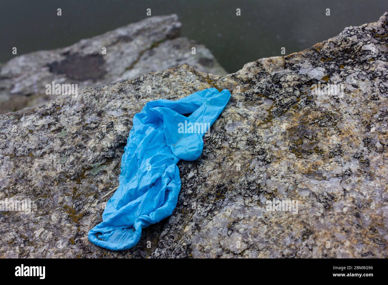 Medizinische Handschuhe auf dem Stein verwendet. Der blaue, zerknitterte Einweghandschuh, der auf den Boden geworfen wird, stellt Gesundheitsrisiken dar und verschmutzt die Umwelt Stockfoto