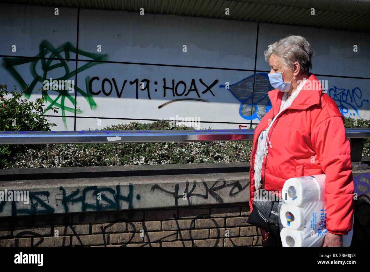 London, Großbritannien. Eine Frau, die eine Toilettenrolle trägt und Gesichtsbezüge trägt, kann man sehen, wie sie inmitten der kovidischen Weltkrise an den 'covid- 19-Falschgraffiti' vorbeigeht. Stockfoto