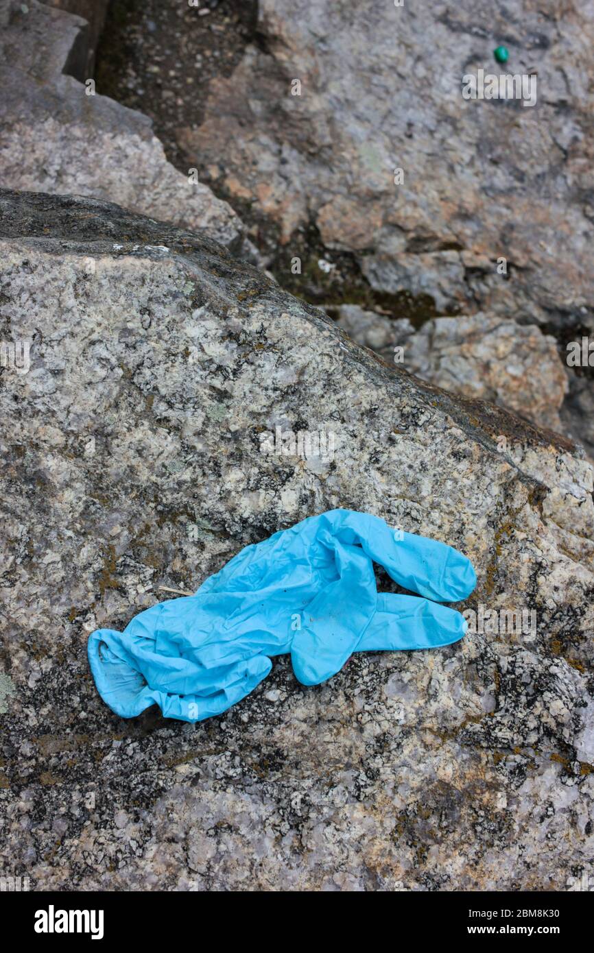 Medizinische Handschuhe auf dem Stein verwendet. Der blaue, zerknitterte Einweghandschuh, der auf den Boden geworfen wird, stellt Gesundheitsrisiken dar und verschmutzt die Umwelt Stockfoto