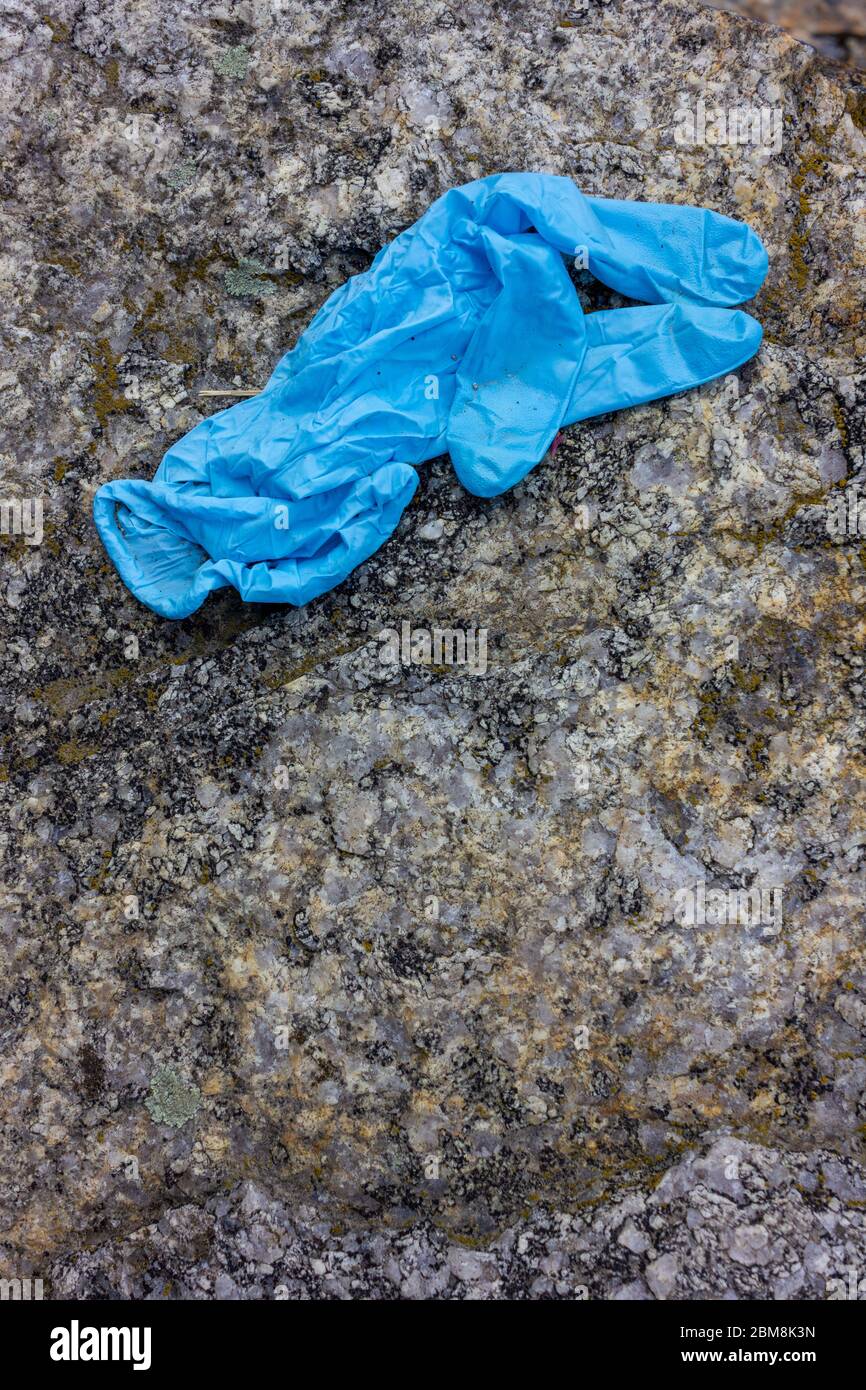 Medizinische Handschuhe auf dem Stein verwendet. Der blaue, zerknitterte Einweghandschuh, der auf den Boden geworfen wird, stellt Gesundheitsrisiken dar und verschmutzt die Umwelt Stockfoto