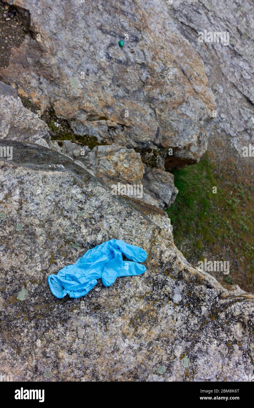 Medizinische Handschuhe auf dem Stein verwendet. Der blaue, zerknitterte Einweghandschuh, der auf den Boden geworfen wird, stellt Gesundheitsrisiken dar und verschmutzt die Umwelt Stockfoto