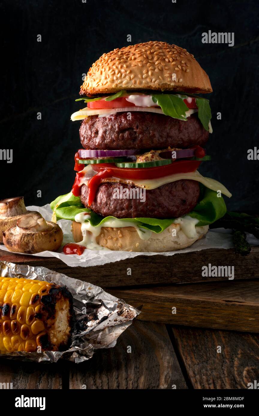 Hausgemachter Burger mit Sesambrötchen, gegrilltem Rindfleisch, Sauce, Gemüse und Käse, garniert mit gerösteten Pilzen. Rustikaler Hintergrund. Kopierbereich. Stockfoto