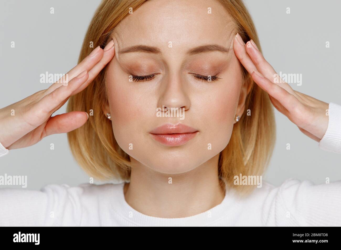 Frau meditiert und massiert ihre Schläfen, schließt die Augen, lindert emotionalen Stress und nervöse Anspannung, erschöpft von Überarbeit, isoliert auf grauem Rücken Stockfoto