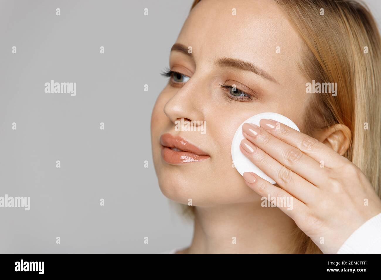 Junge blonde junge Frau Reinigung (Entfernen Make-up) ihr Gesicht mit Wattepad, isoliert auf grauem Hintergrund, kopieren Raum. Gesunde Hautpflege, Gesichtsbehandlung Stockfoto