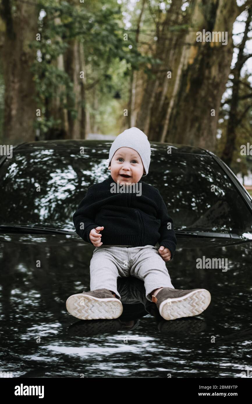 Niedlicher 1-jähriger Junge mit schönen Augen, der auf dem Auto sitzt und die Kamera anschaut Stockfoto