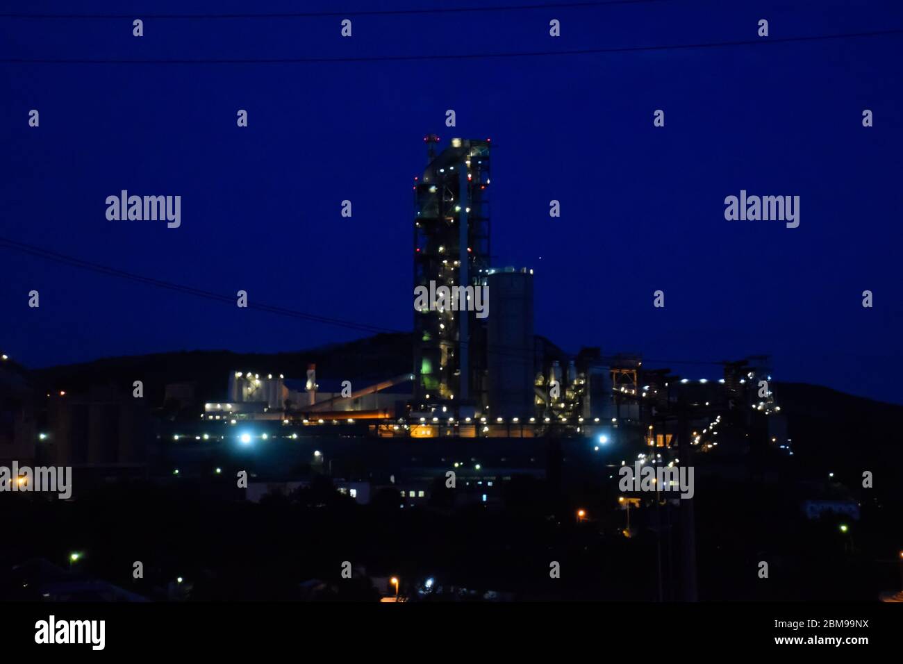 Das Gebäude einer Zementfabrik in der Nacht, die Lichter einer Lampe, die eine Fabrik beleuchtet. Industrieanlage. Stockfoto