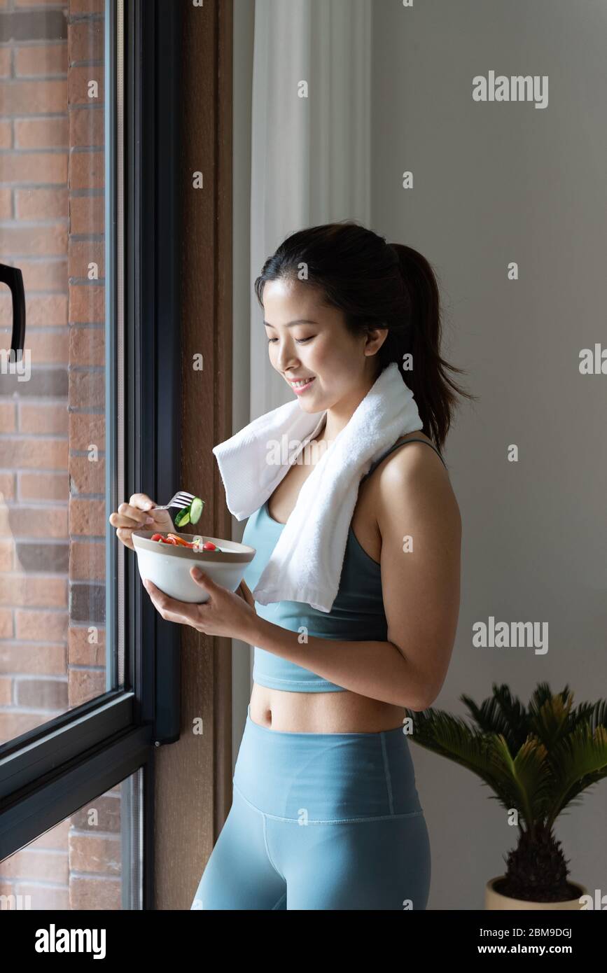 Eine junge asiatische Frau, die gesundes grünes Gemüse am Fenster isst Stockfoto