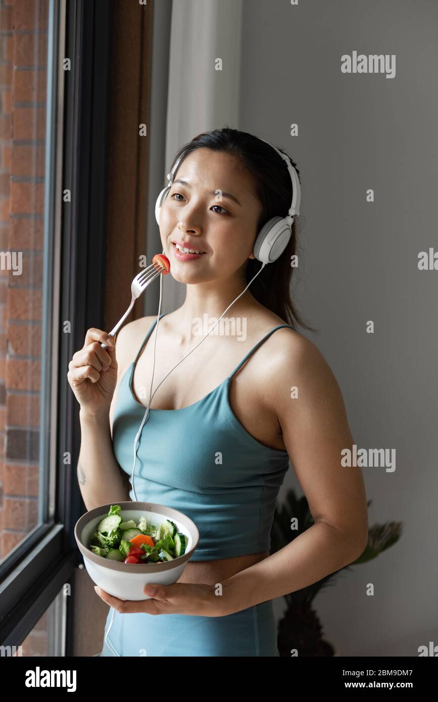 Eine junge asiatische Frau, die gesundes grünes Gemüse am Fenster isst Stockfoto