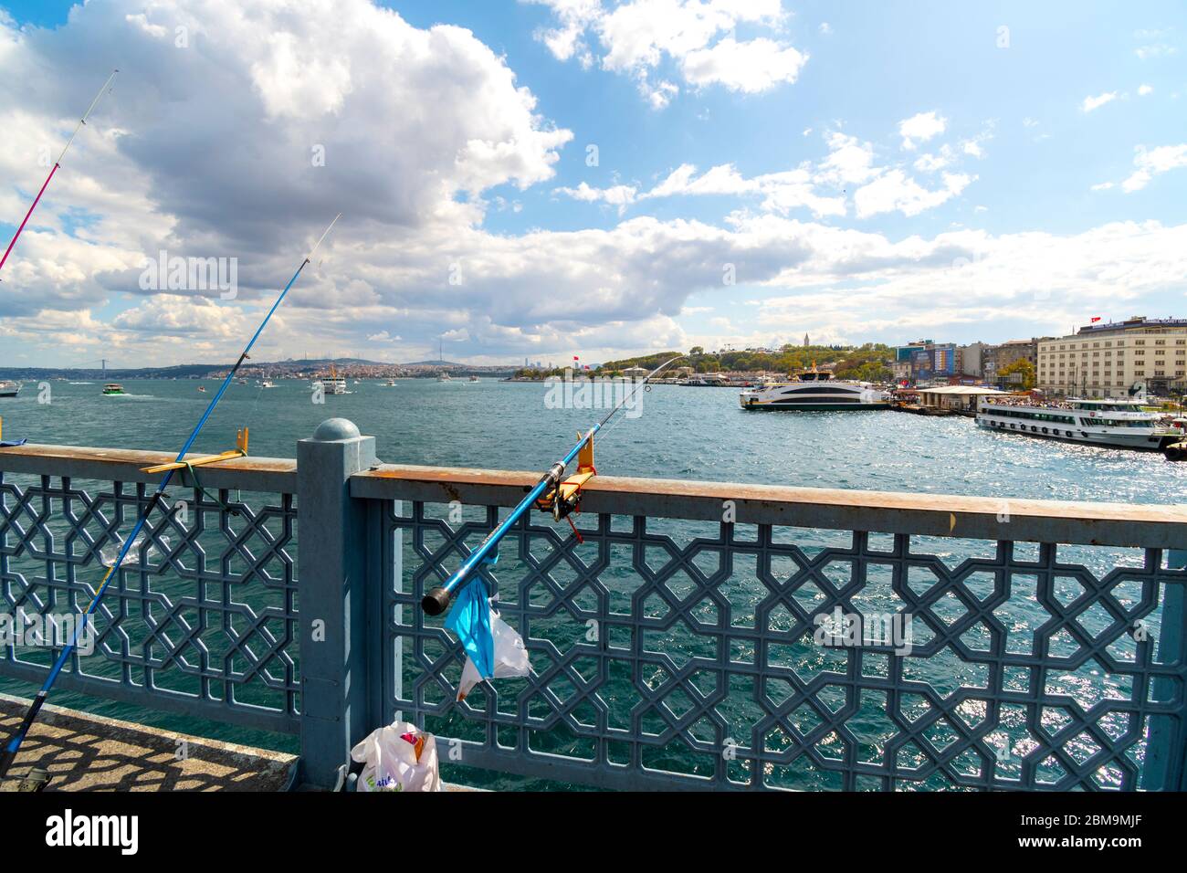 Angelstangen und Angelschnur ragen über den Bosporus von der Galata Brücke, während eine Kreuzfahrt Tour Boote in der Nähe in Istanbul, Türkei andocken Stockfoto