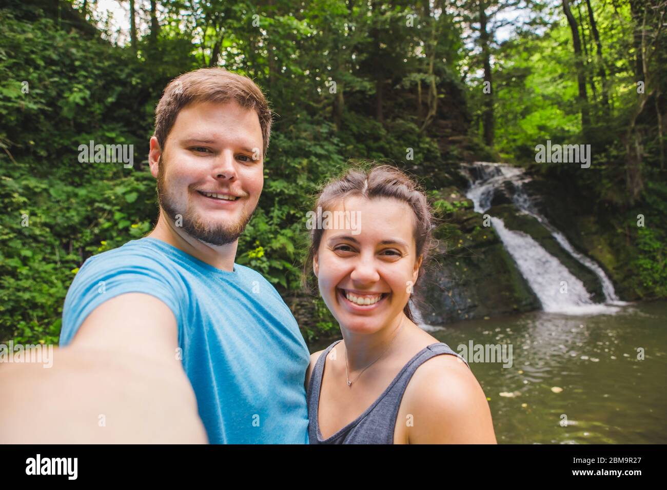 Lächelndes Paar, das Selfie vor einem Wasserfall im Wald nimmt Stockfoto
