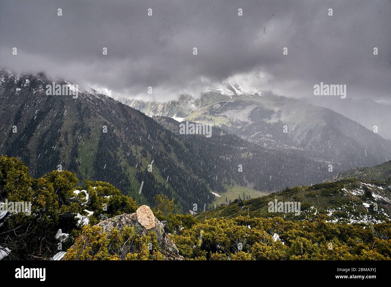 Heavy Rain am Berge mit dunklen Wolken und schneebedeckten Gipfel Stockfoto