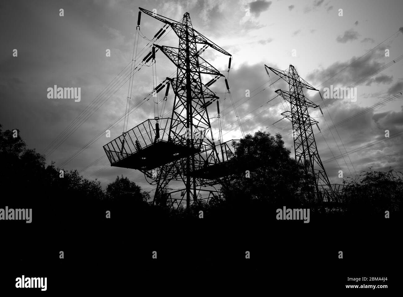 Ein silhouetted Paar Strom pylon Türme hinter einer Baumgrenze mit einem launisch aussehenden Himmel und Wolken Stockfoto