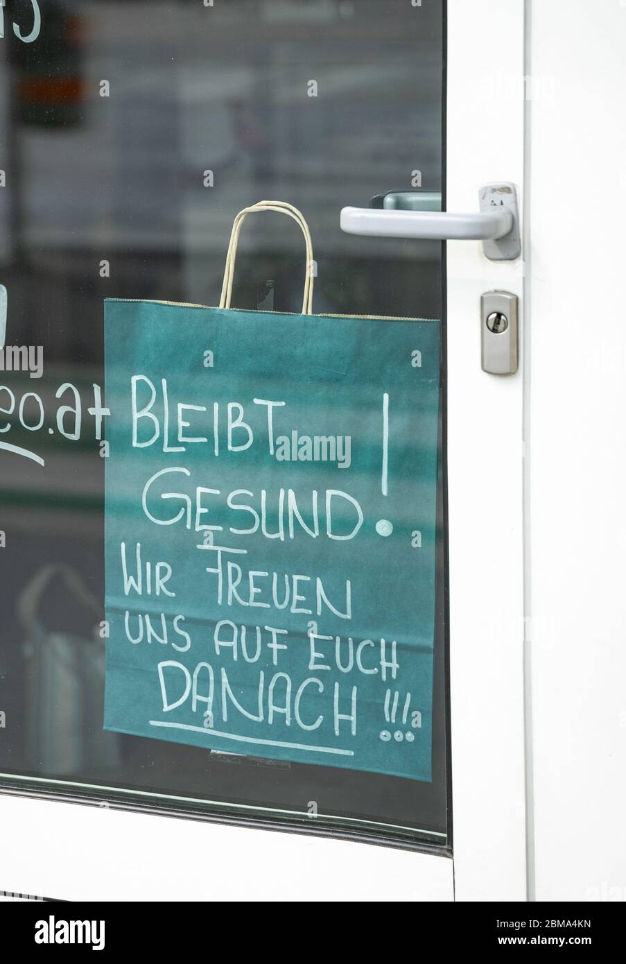 Bleiben Sie gesund Wunsch, geschrieben in deutscher Sprache auf einem Papier-Einkaufstasche und aufgehängt in einem Ladeneingang Stockfoto