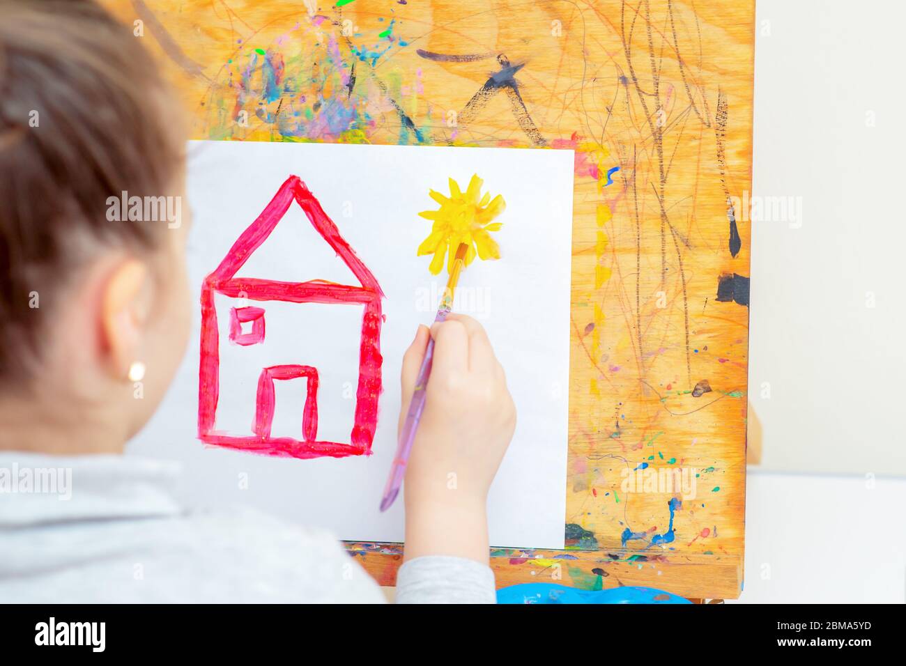 Hand des Kindes Zeichnung gelbe Sonne und rotes Haus mit Pinsel auf Blatt Papier in der Schule. Mädchen Zeichnung mit Aquarellen. Stockfoto