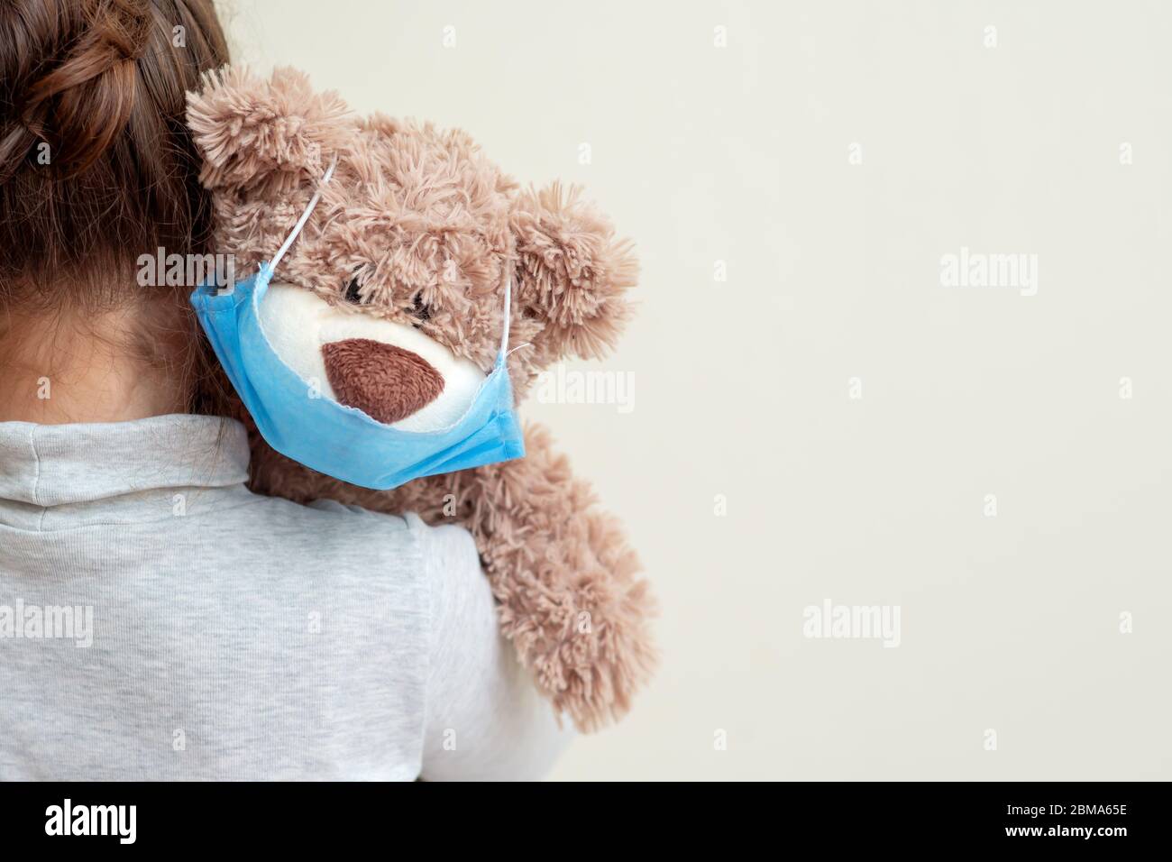 Plüschbär mit schützender medizinischer Maske auf der Schulter des Kindes. Gesundheitsfürsorge und Virenschutz. Stockfoto